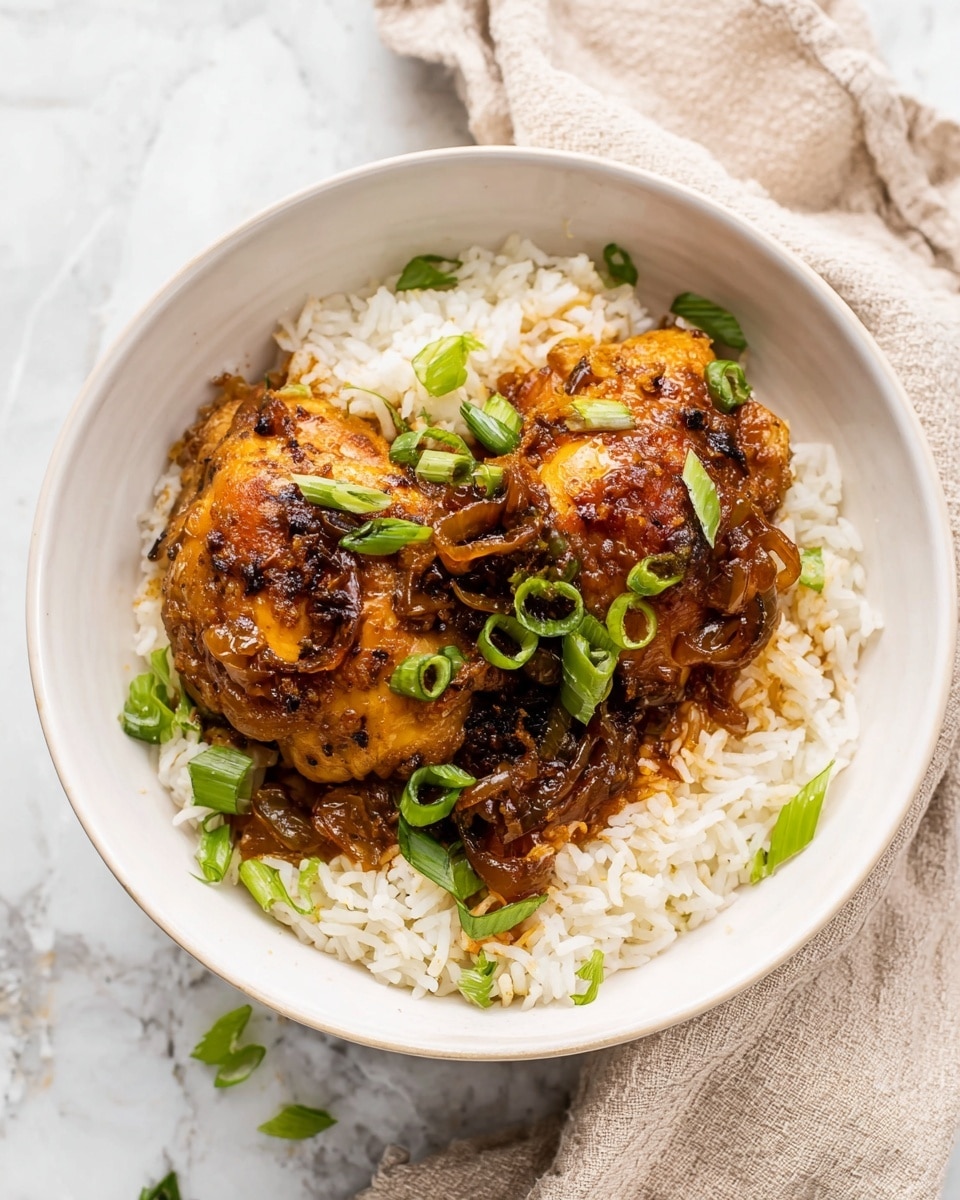 A white bowl filled with a base layer of white cooked rice that looks soft and fluffy. On top of the rice, there are two pieces of cooked chicken thighs covered with a rich, glossy brown sauce that has visible caramelized onion slices. The chicken pieces are garnished with sliced green onions, adding a fresh pop of green color. The bowl rests on a white marbled surface, beside a light beige cloth napkin. Photo taken with an iphone --ar 4:5 --v 7