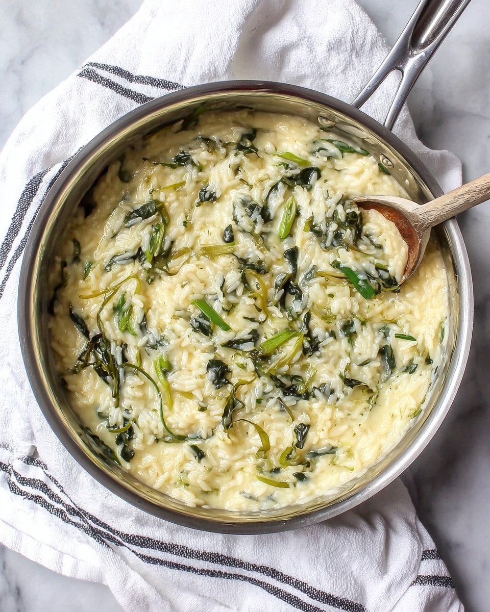 A large silver pan filled with creamy yellow rice mixed with dark green and light green leafy vegetables. The rice looks soft and moist, with a thick texture that holds the leaves and small vegetable pieces well. The pan is placed on a white cloth with thin black stripes, which lies on a white marbled surface. photo taken with an iphone --ar 4:5 --v 7