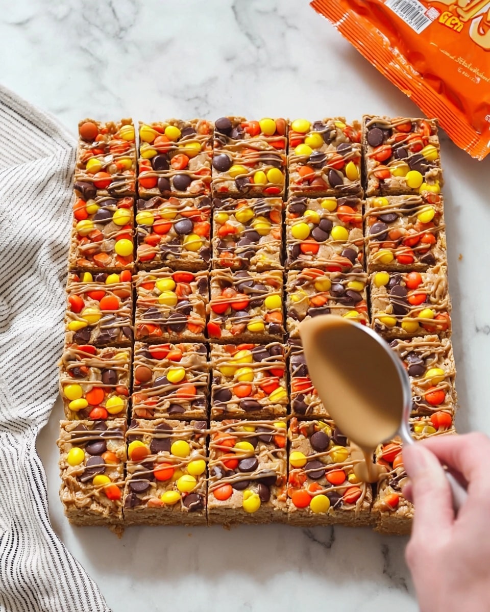 A large square of dessert bars made of a golden brown cookie base, cut into 20 small rectangles arranged in 5 rows and 4 columns. The top layer is covered with bright candy pieces in orange, yellow, and dark brown colors, scattered evenly. There is a drizzle of light brown sauce on top, being poured from a silver spoon held by a woman's hand at the right side. The dessert sits on a white marbled surface with a white and gray striped cloth slightly visible in the top left corner and a partially opened bright orange candy bag at the top right. photo taken with an iphone --ar 4:5 --v 7