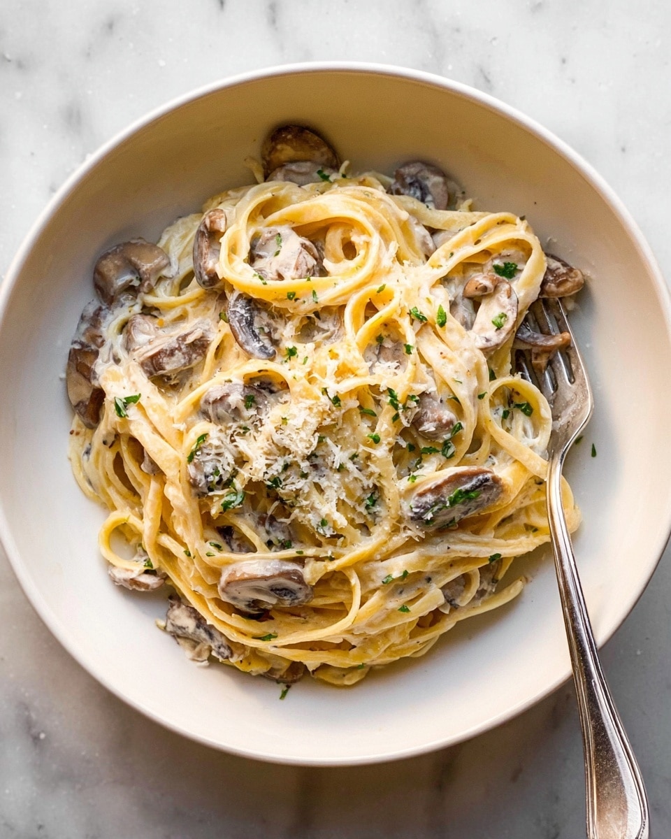 A large red pot with cream-colored inside holds a creamy pasta dish with about three main layers: a thick white sauce with specks of green herbs spread around the bottom, thin flat noodles mixed evenly in the center, and sliced light brown mushrooms scattered throughout and on top of the noodles. Some shredded cheese and small red chili flakes are sprinkled over the pasta, adding texture and color. Metal tongs rest in the pot, holding some noodles in place. The pot sits on a white marbled surface, and a beige cloth with dark stripes is softly draped near the top. Photo taken with an iphone --ar 4:5 --v 7