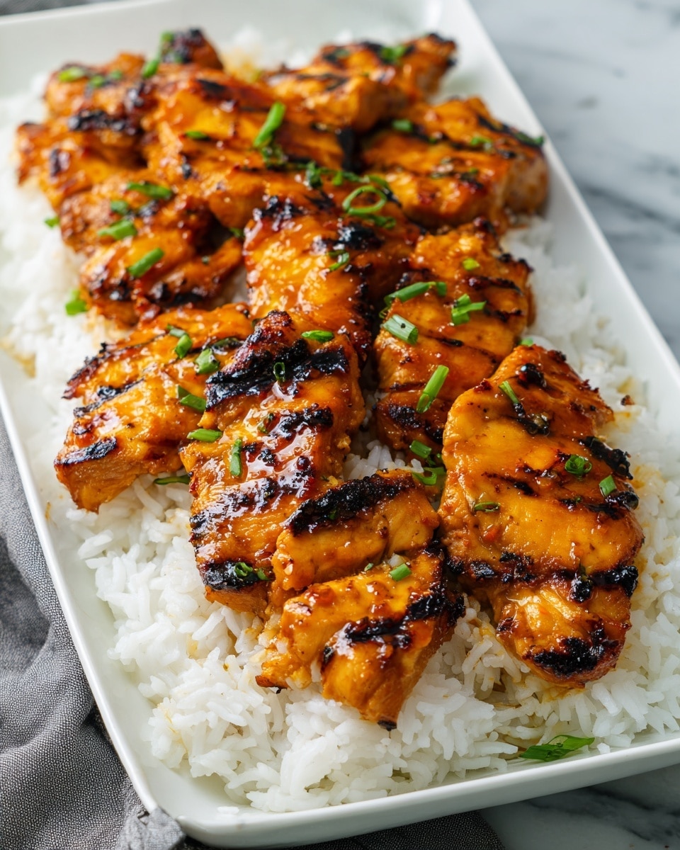 A rectangular white bowl filled with a base layer of fluffy white rice, topped with eight pieces of grilled chicken glazed in a shiny, dark orange-brown sauce with charred spots. The chicken pieces are arranged closely in two rows, with small green chive bits sprinkled on top. The bowl sits on a white marbled surface with a gray cloth partially visible beside it photo taken with an iphone --ar 4:5 --v 7