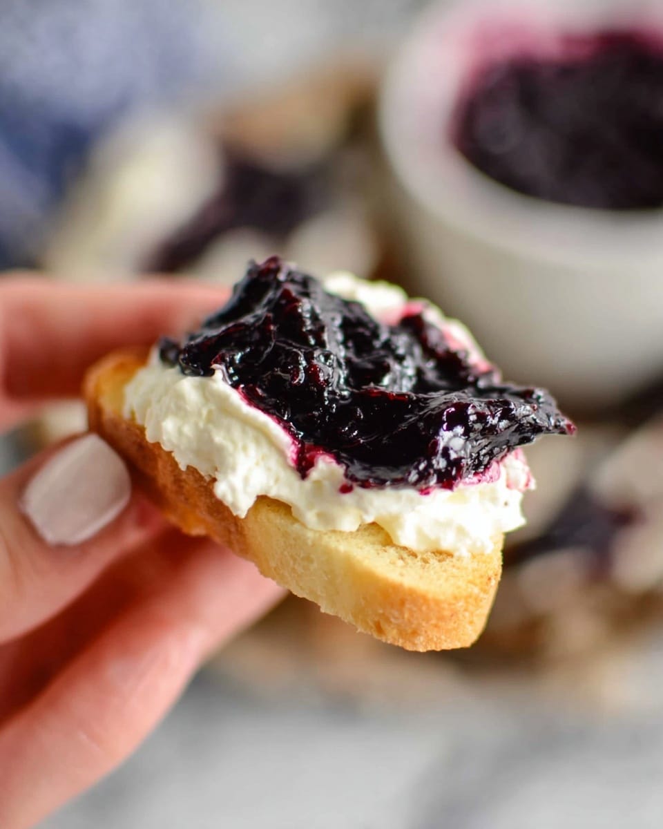 A close-up view shows a woman's hand holding a piece of torn bread topped with a thick, creamy spread that has swirls of purple and white colors. The spread looks soft and mixed with dark purple fruit bits, giving it a marbled texture. A knife with purple spread on its edge is pressing against the bread. The background is softly blurred with a white marbled surface faintly visible below. photo taken with an iphone --ar 4:5 --v 7