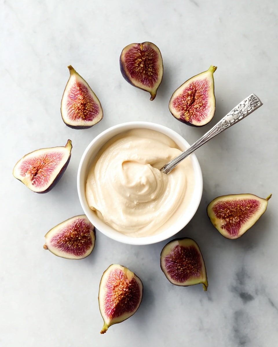 A small white bowl filled with creamy, smooth light beige yogurt sits in the center on a white marbled surface. A silver spoon with an ornate handle is placed inside the yogurt. Around the bowl, there are several halves of fresh figs with dark purple skin and bright pink, textured interiors scattered in a loose circular pattern. The scene is bright and clean, with natural light highlighting the creamy texture of the yogurt and the fresh juicy details of the figs. Photo taken with an iphone --ar 4:5 --v 7