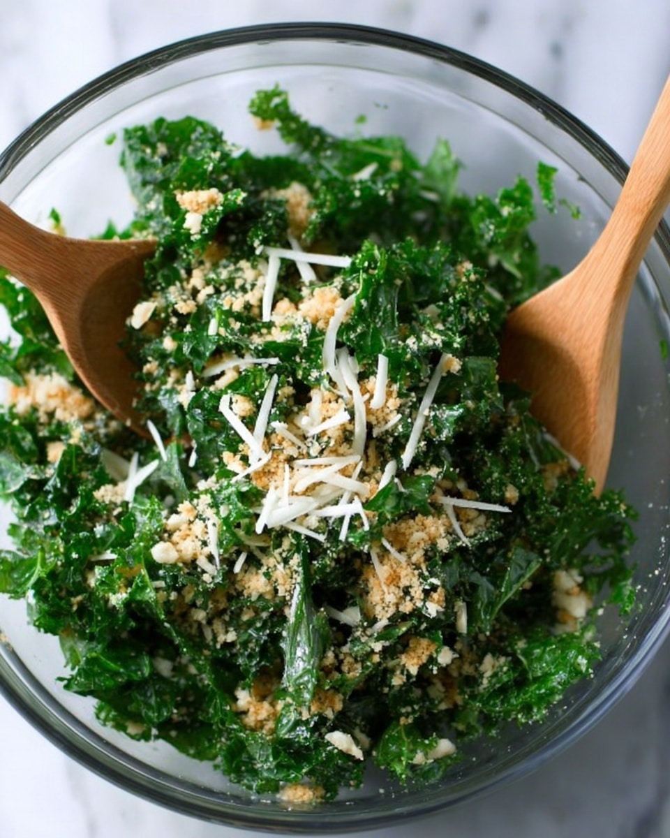 A clear glass bowl filled with a fresh kale salad is shown on a white marbled surface. The salad has roughly torn dark green kale leaves mixed with small light brown breadcrumbs and thin white shreds of cheese scattered evenly on top. Two small wooden spoons are placed inside the bowl, one positioned on the left side and the other on the right, both slightly lifting the salad. The texture of the kale looks crisp and leafy, while the breadcrumbs add a crumbly touch and the cheese shreds add contrast to the greens. Photo taken with an iphone --ar 4:5 --v 7