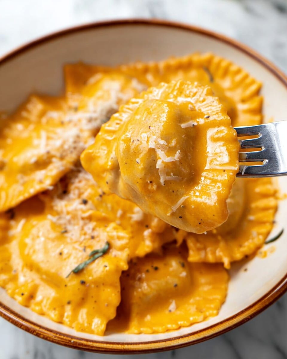 A close-up view of several ravioli pieces covered in a thick orange sauce, arranged in a slightly overlapping pile inside a white bowl with blue decorative patterns. The ravioli have soft curved edges with some texture visible on the pasta, and the sauce looks creamy and smooth with black pepper sprinkled across. On top of the ravioli, there is a small mound of shredded white cheese adding texture contrast. The bowl is placed on a white marbled surface. photo taken with an iphone --ar 4:5 --v 7