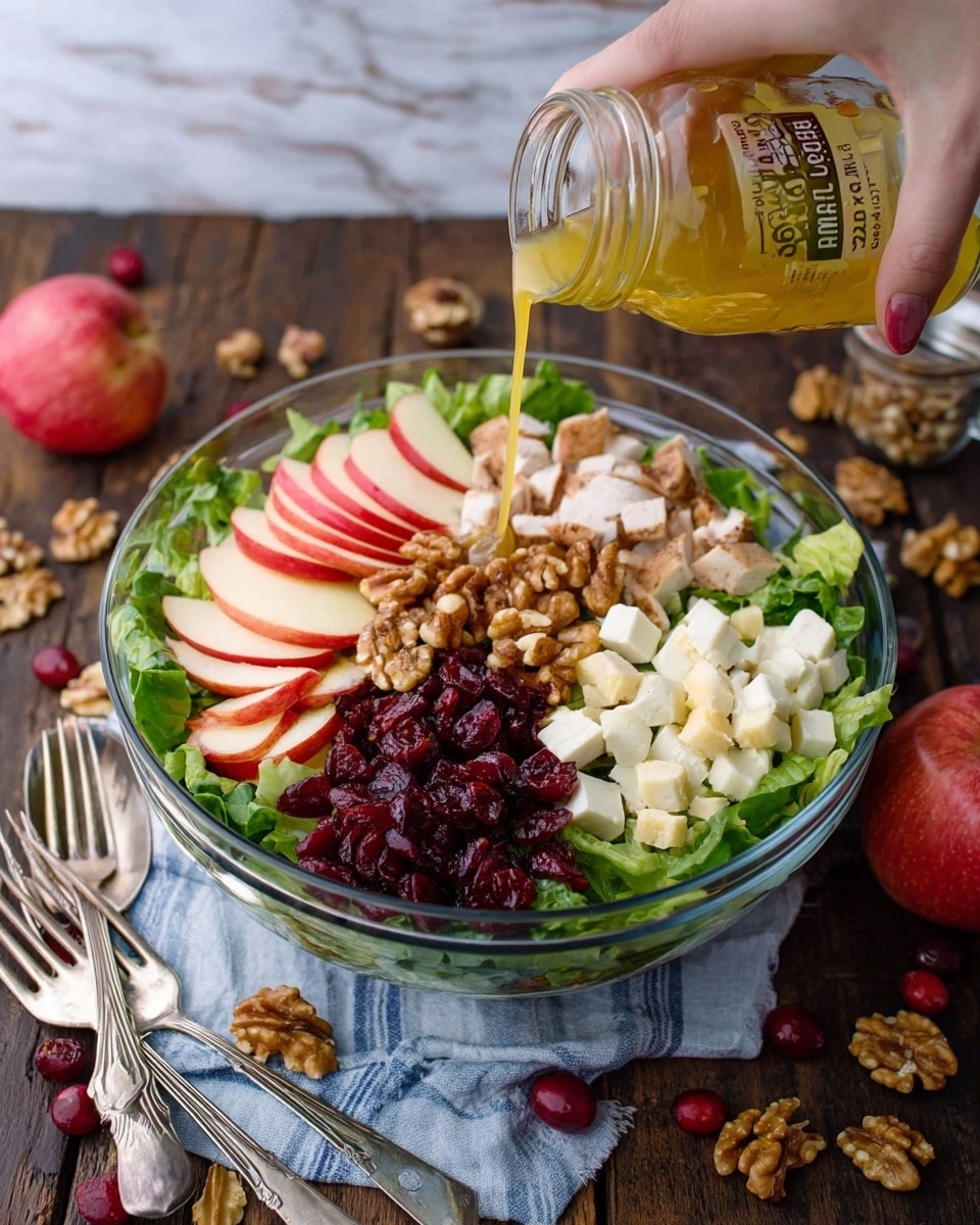 A clear glass bowl sits on a white marbled surface with a fresh salad inside. The salad has a base of green leafy lettuce. On top, there are six layers arranged in sections: cubed pale turkey at the top right, light yellow cheese cubes below the turkey, dark red dried cranberries beneath the cheese, light brown walnut halves on the bottom left, thinly sliced white pears with brown edges above the walnuts, and red apple slices with white inside at the top left. Around the bowl, some walnuts and dried cranberries are scattered on the white marbled background, and a whole red apple is placed near the bottom right. A blue and white striped cloth is partly visible behind the bowl. photo taken with an iphone --ar 4:5 --v 7