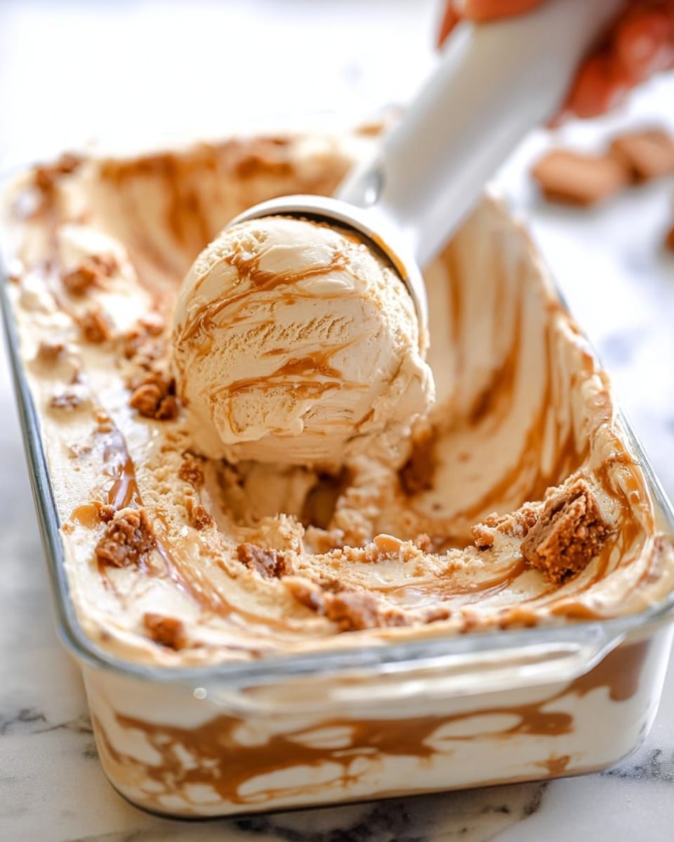 This image shows a close-up of a rectangular glass container filled with creamy textured ice cream mixed with chunks of brown toffee or cookie pieces on a white marbled surface. The ice cream has a light beige color with thick swirls of caramel-colored sauce on top, creating a rich marbled effect. A white ice cream scooper held by a woman's hand lifts a rounded scoop from the container, showing layers of smooth ice cream and crunchy bits throughout. The background is softly blurred, highlighting the creamy texture and colors of the ice cream. photo taken with an iphone --ar 4:5 --v 7