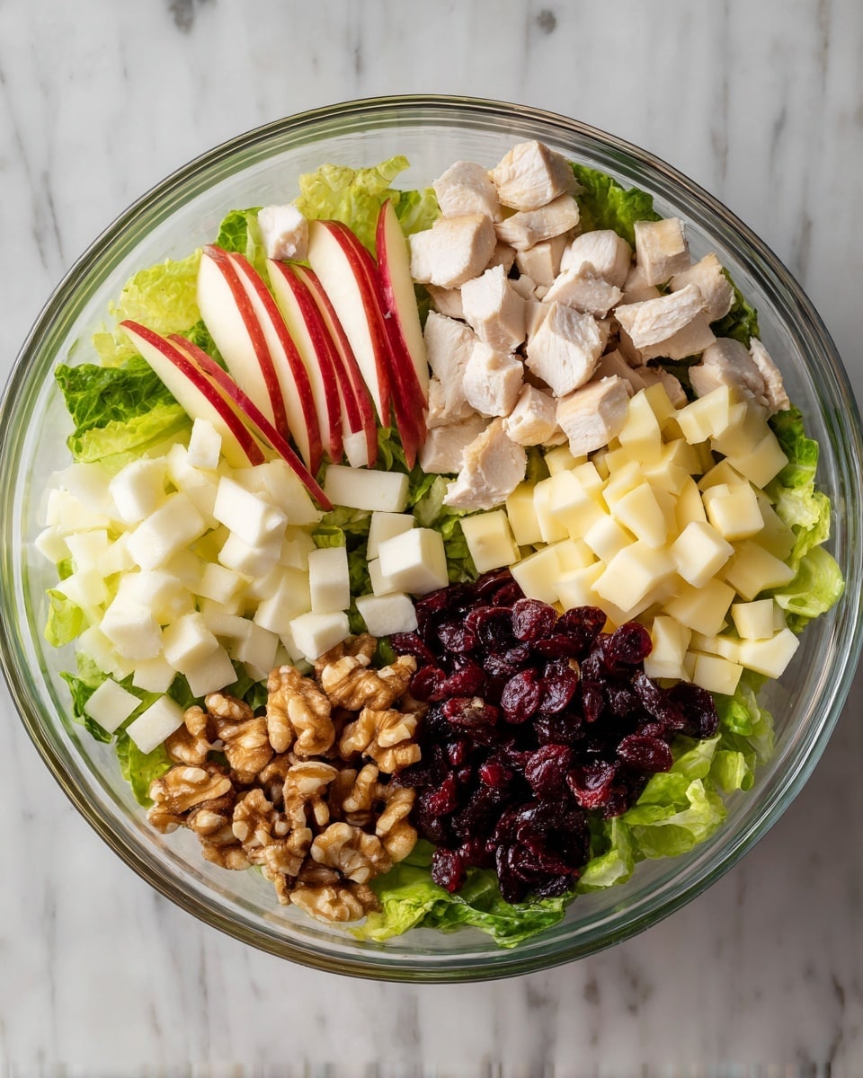 A clear glass bowl filled with layers of fresh green lettuce at the bottom, topped with five sections of ingredients neatly arranged: sliced red apple on the left, light brown walnuts next to it, dark red dried cranberries in the center, white cheese cubes to the right, and diced light beige cooked chicken pieces on the far right. Above the bowl, a woman's hand pours a golden yellow dressing from a small glass jar over the cranberries. The bowl sits on a dark wooden table with scattered walnuts and dried cranberries around it, a whole red apple on the lower right, and three vintage silver forks to the left on a blue and white striped cloth. The background has a white marbled texture. photo taken with an iphone --ar 4:5 --v 7