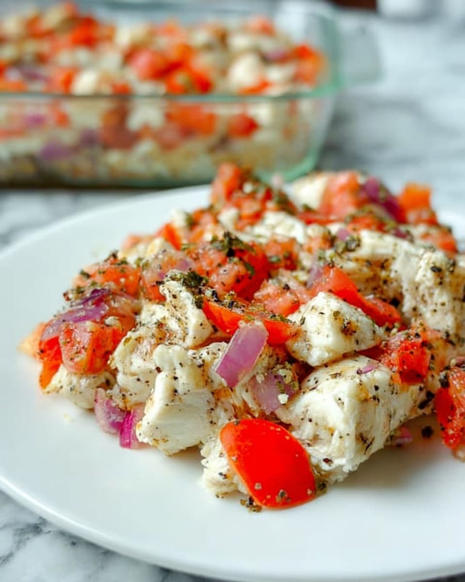 The image shows a close-up of a dish served on a white plate placed on a white marbled surface. The dish has three main layers: a base layer of soft, white chunks of cooked chicken, topped with a mix of finely chopped red tomatoes and small pieces of red onion, sprinkled with black pepper and green herbs. The ingredients are mixed but still distinguishable, with the red tomatoes and purple onion pieces standing out against the pale chicken, giving a fresh and light look. In the background, a glass dish with more of the same food is visible, slightly blurred. photo taken with an iphone --ar 4:5 --v 7