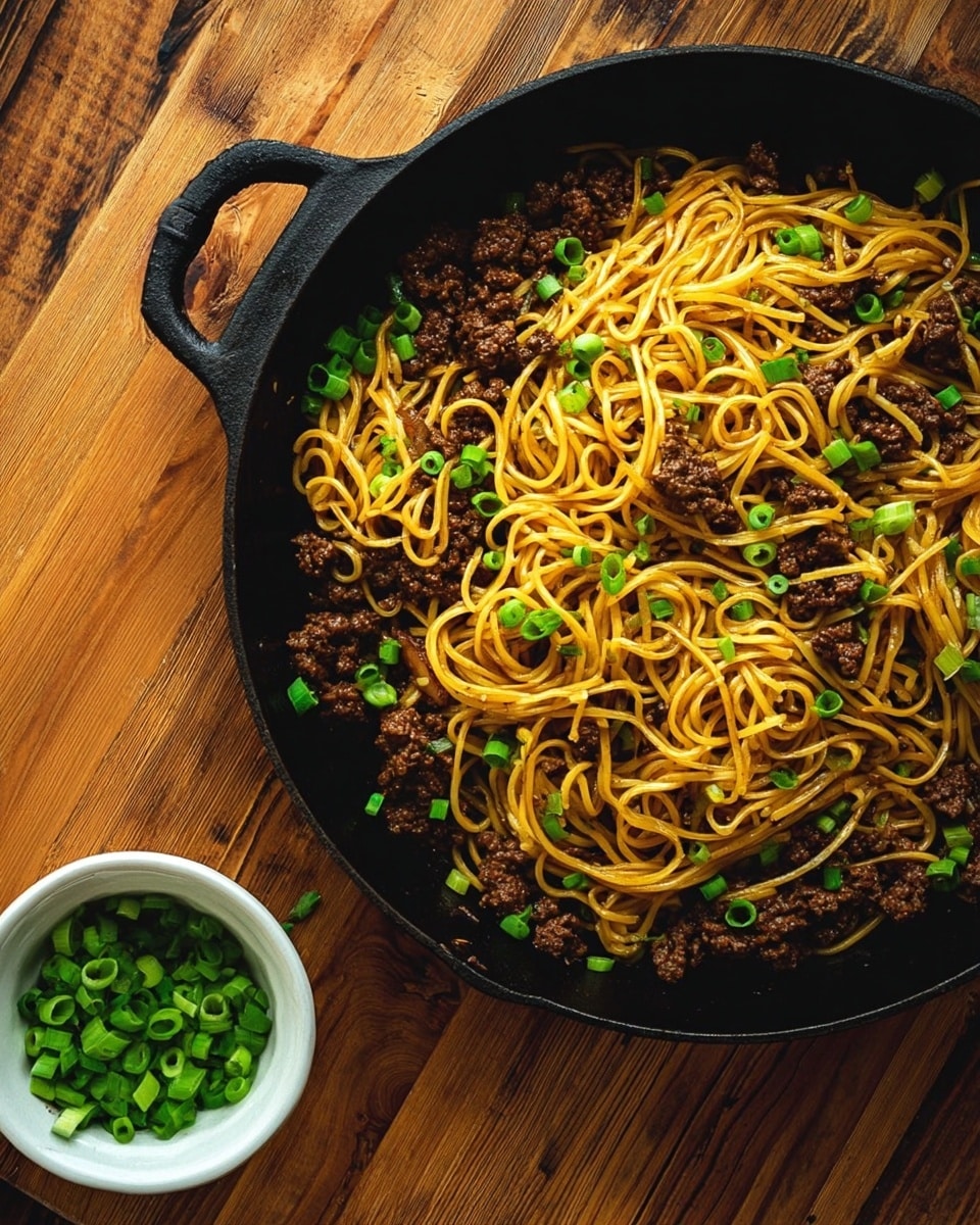 A black cast iron pan filled with a single layer of golden yellow noodles mixed evenly with small pieces of dark brown cooked meat, all topped with scattered bright green chopped scallions, sits on a wooden table. Next to the pan, there is a small white bowl filled with more chopped scallions. The table has a natural wooden texture, and the whole scene is lit warmly. Photo taken with an iphone --ar 4:5 --v 7