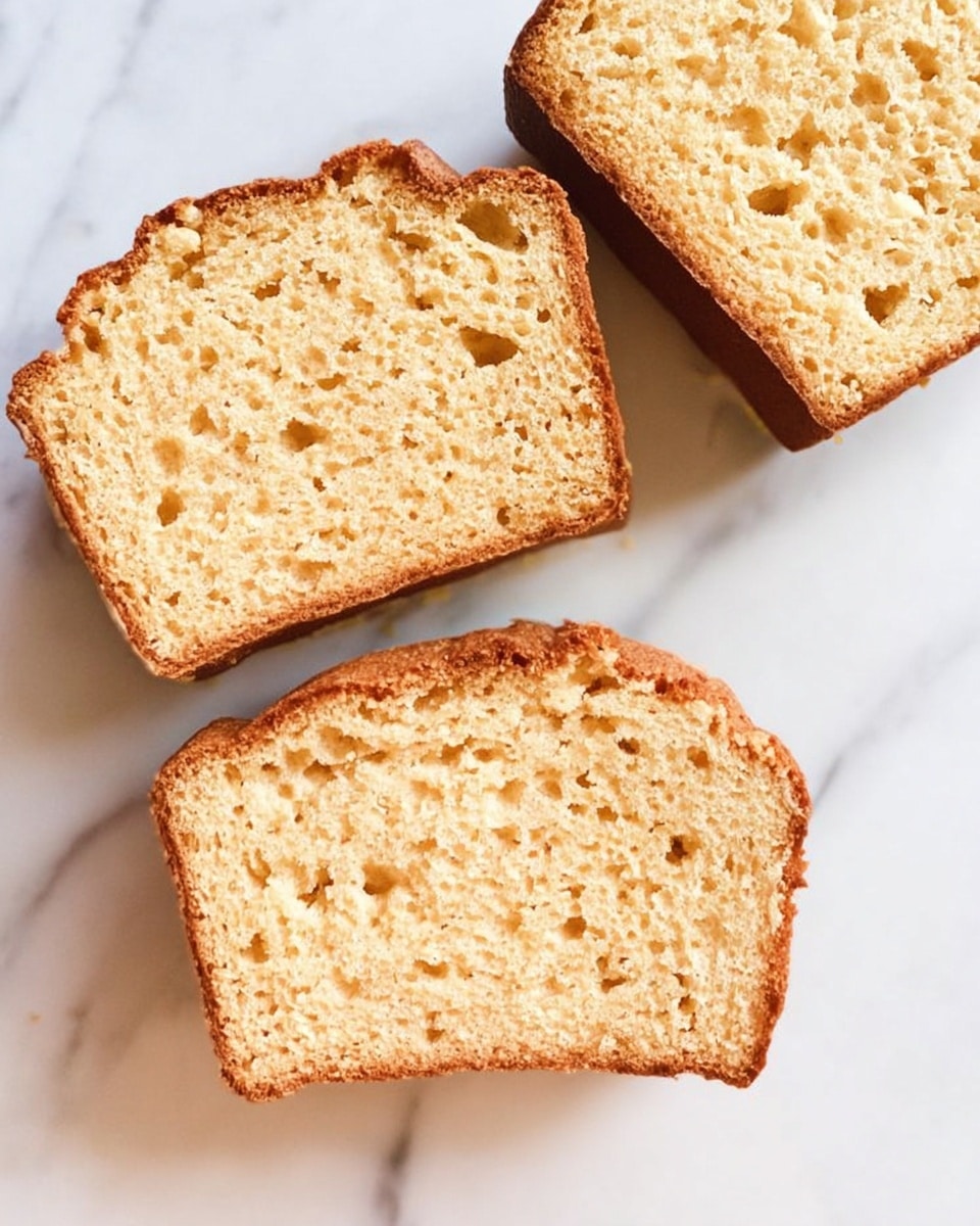 Three slices of light golden brown bread with a spongy, airy texture are placed on a white marbled surface. Each slice shows a soft crumb with small holes inside and a slightly darker crust around the edges. The slices are arranged loosely, not touching each other. The top slice is whole, while the other two have uneven edges, showing a natural, homemade look. photo taken with an iphone --ar 4:5 --v 7