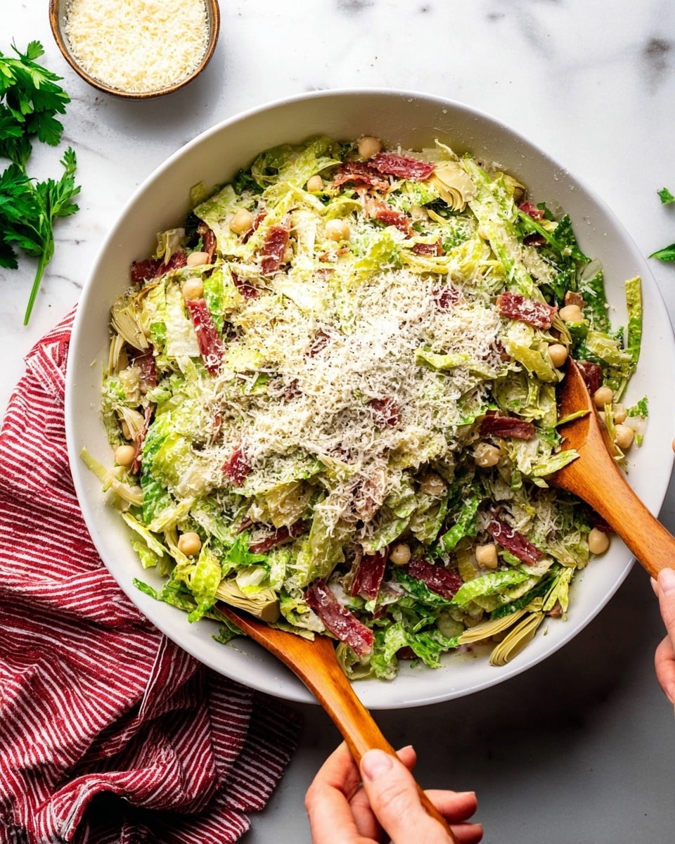 A large white bowl filled with a fresh mixed salad showing visible layers of shredded light green lettuce as the base, scattered with thin strips of reddish cured meat, artichoke hearts in pale green, and a sprinkling of beige chickpeas. The top layer is a generous dusting of grated white cheese, contrasting with the bright greens and reds. Two wooden salad spoons are being held by a woman's hand on the right and another woman's hand on the left, lifting and mixing the salad. The bowl is placed on a white marbled surface with a small bowl of grated cheese and a sprig of parsley in the background, along with a red and white striped cloth near the bottom of the image. Photo taken with an iphone --ar 4:5 --v 7