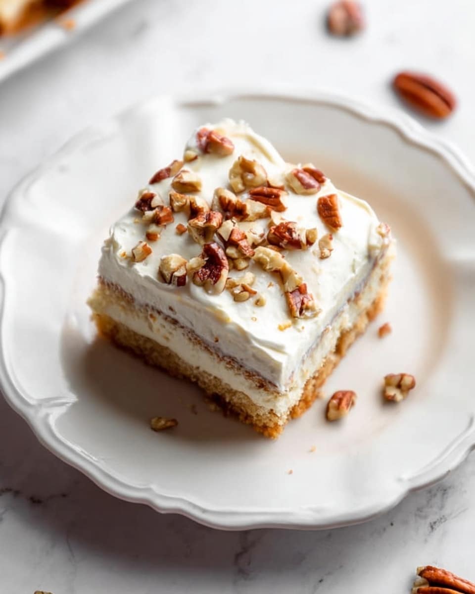 A single square piece of cake is shown on a white plate with a wavy rim. The cake has three visible layers: the bottom layer is a light brown, soft-looking cake; the middle layer is a thick, creamy white filling; and the top layer is white frosting, spread evenly with a smooth but slightly textured surface. On top of the frosting, there are small pieces of chopped pecans scattered, showing a mix of light brown and darker brown colors. The plate sits on a white marbled surface, with a few pecan pieces scattered around the plate. photo taken with an iphone --ar 4:5 --v 7