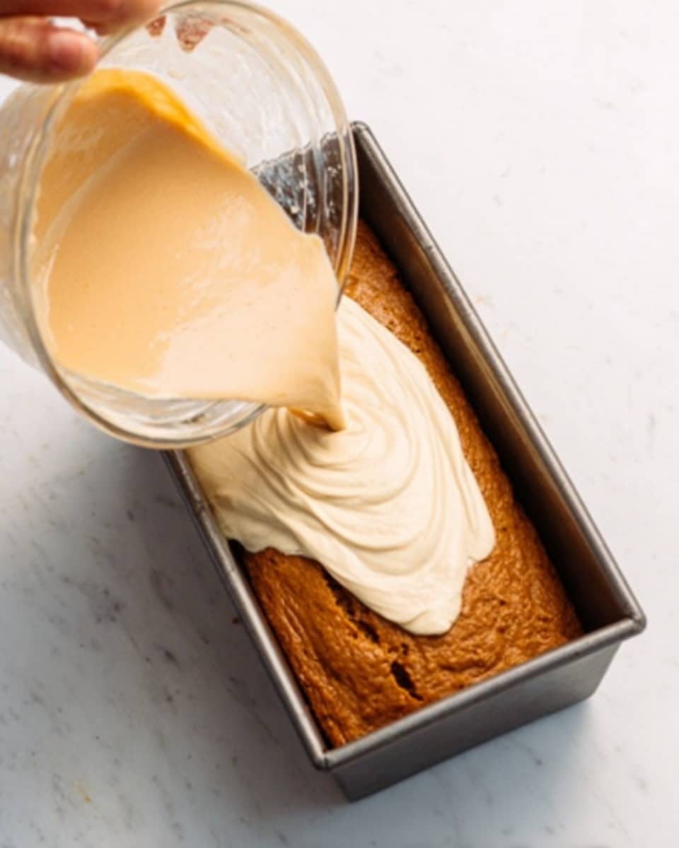 The image shows a rectangular metal loaf pan on a white marbled surface filled halfway with a thick brown batter. A woman’s hand is holding a clear bowl tilted over the pan, pouring a smooth, pale cream-colored batter in an uneven layer on top of the brown batter. The two batters have different textures, with the brown one looking denser and the cream one lighter and flowing. Photo taken with an iphone --ar 4:5 --v 7