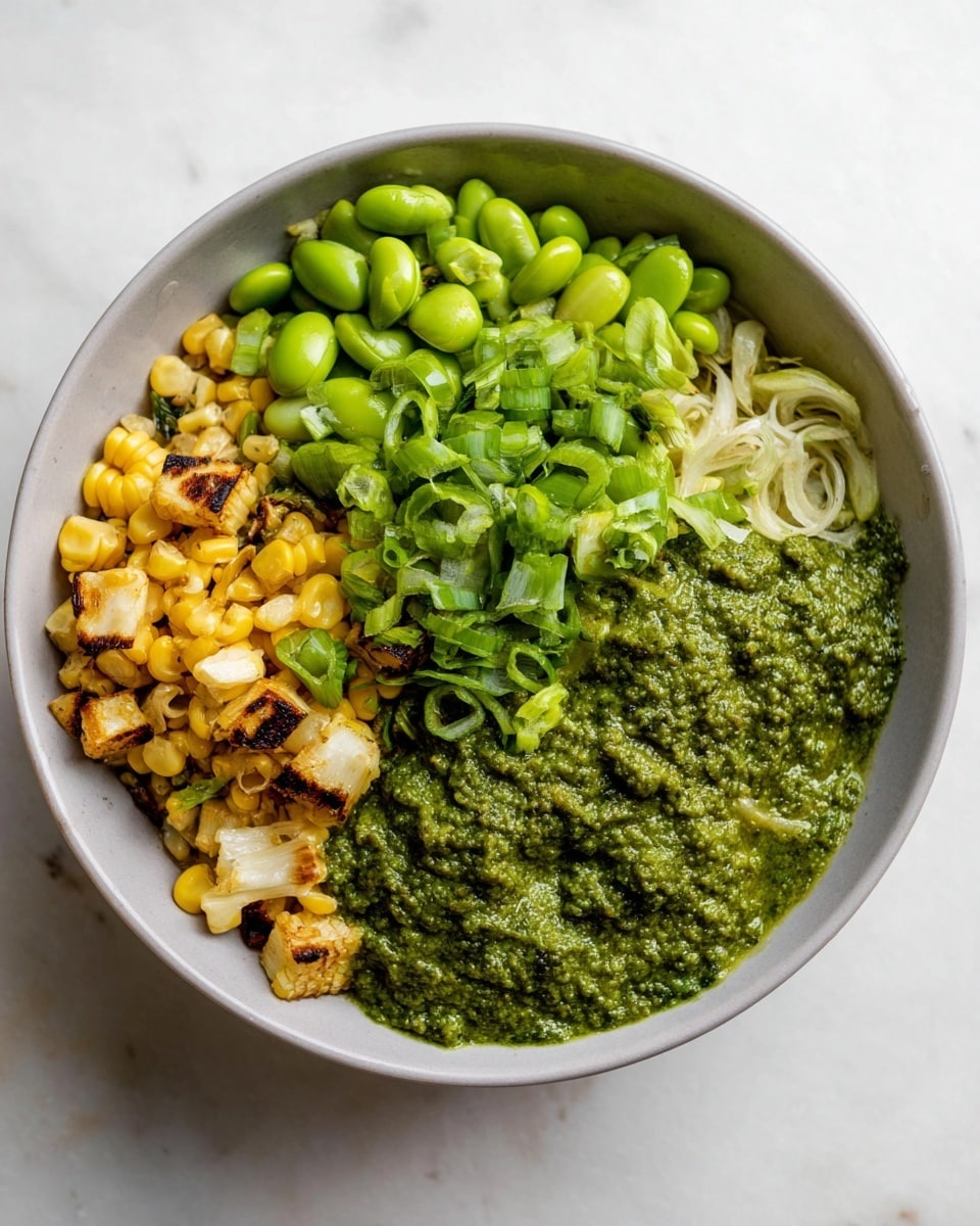A white bowl holds a food dish with four main parts. On the bottom left, there are small chunks of grilled corn with a yellow and slightly brown color. Next to the corn, towards the top left, is a pile of bright green soybeans. On the top right, there are thinly sliced green onions, light and dark green in color. Covering the middle to the right side of the bowl is a thick green sauce with a rough texture. The bowl is set on a white marbled surface. photo taken with an iphone --ar 4:5 --v 7