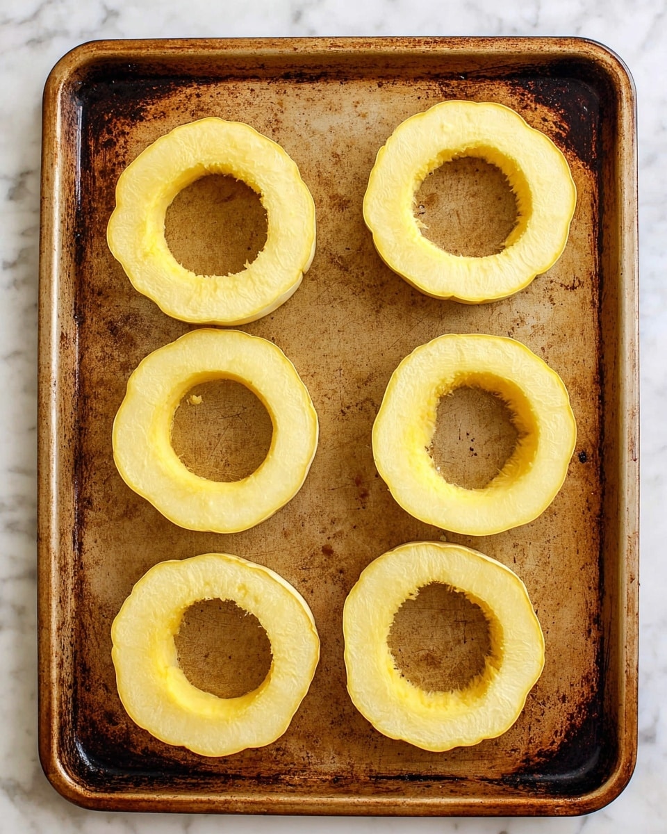 The image shows six pale yellow, ring-shaped squash slices arranged evenly on a large, well-used baking tray with dark brown spots and scratches. Each slice has a hollow center with slightly uneven edges and a smooth, firm texture. The baking tray sits on a white marbled surface, providing a clean background contrast to the rustic look of the tray and the fresh squash rings photo taken with an iphone --ar 4:5 --v 7