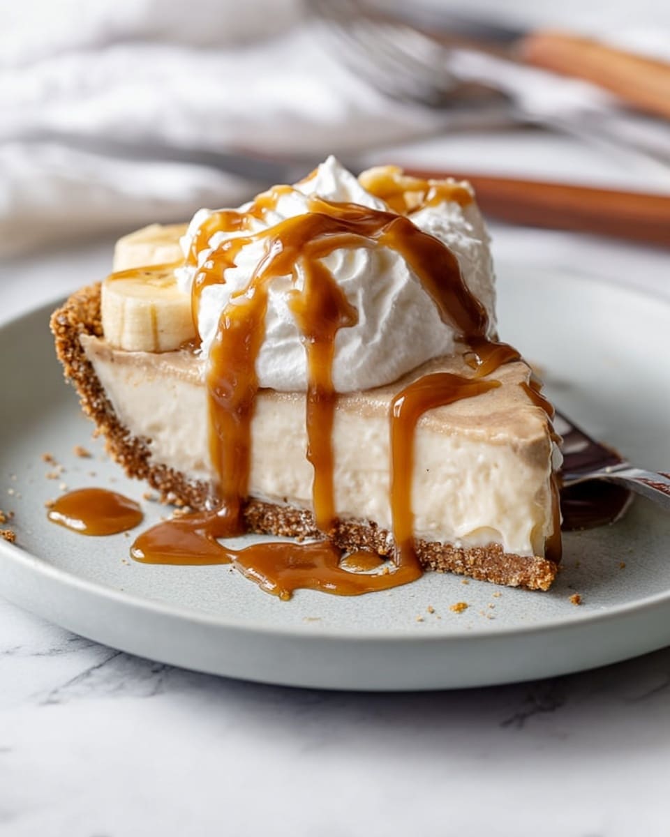 A slice of pie with three layers sits on a light grey plate: the bottom crust is rough and brown, the middle creamy layer is smooth and pale beige, and the top layer features small banana pieces. On top, a large dollop of white whipped cream is covered with glossy brown caramel sauce that drips down the sides and onto the plate. The plate is on a white marbled surface, and a knife and fork rest in the background. Photo taken with an iphone --ar 4:5 --v 7