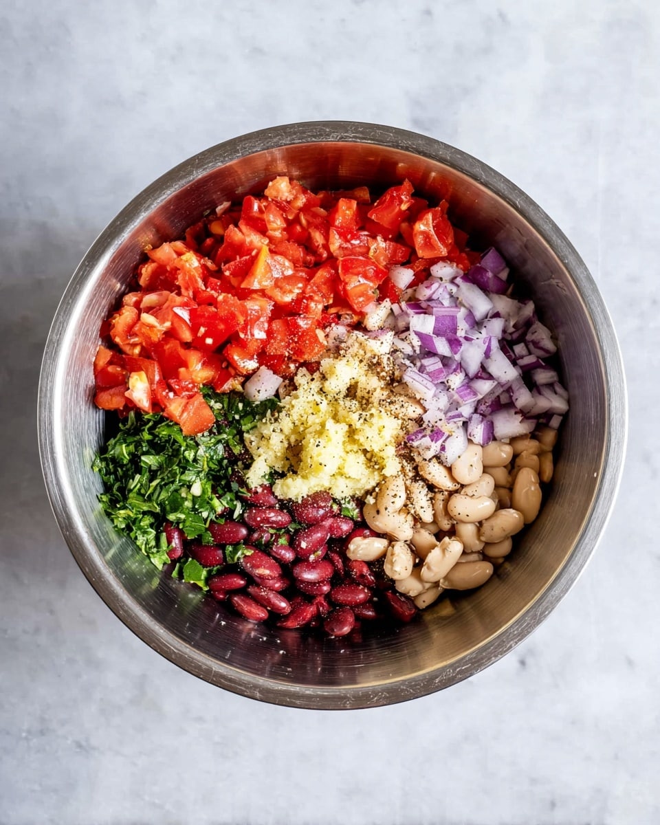 A shiny silver mixing bowl sits on a white marbled surface, filled with six clear layers of ingredients arranged in separate sections. On the upper left, chopped bright red tomatoes form a chunky layer. To the right of the tomatoes, white beans mixed with coarse black pepper create a light beige and black speckled section. Further right, chopped purple onion pieces add a vibrant touch. Below the onions, dark red kidney beans with some purple onion bits make a deep reddish-purple layer. At the bottom left, green chopped leafy herbs provide fresh color, while in the center, a creamy yellow pile of minced garlic adds texture. The ingredients are clearly separated inside the bowl, ready to be mixed. Photo taken with an iphone --ar 4:5 --v 7