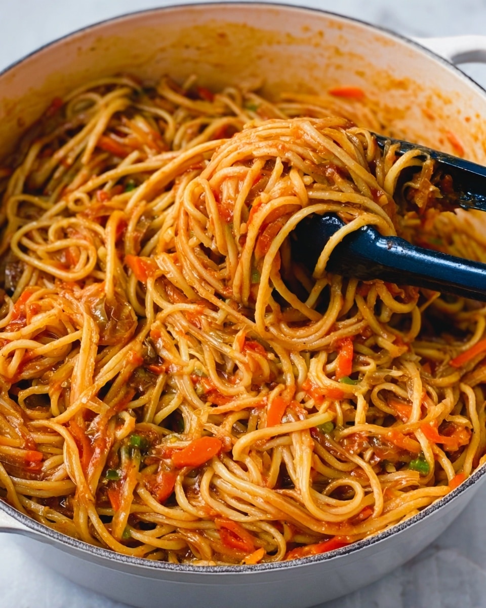 The image shows a close-up of a large white pot filled with spaghetti mixed with a reddish sauce, small pieces of carrots, and bits of green vegetables. The noodles are glossy and appear coated evenly with the sauce, creating a slightly shiny texture. A pair of black tongs is lifting a portion of the pasta from the pot, with the noodles twisted around them, revealing the thick sauce clinging to the strands. The pot sits on a white marbled surface, adding a clean and bright background to the warm colors of the pasta dish. photo taken with an iphone --ar 4:5 --v 7