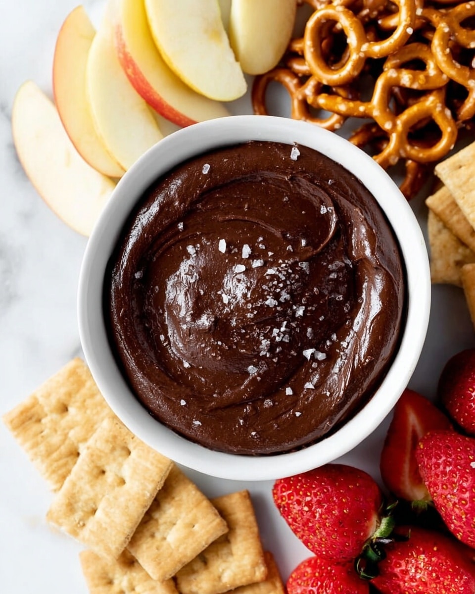 A white bowl full of thick, dark brown chocolate dip with a shiny, smooth texture and a sprinkle of coarse salt on top sits in the center of the image. Around the bowl, on a white marbled surface, there are four layers arranged in separate groups: pale yellow sliced apples on the top left, light brown crunchy pretzels on the top right, beige rectangular graham crackers on the bottom left, and bright red strawberries, some whole and some sliced in half, on the bottom right. The whole scene is bright and clean. photo taken with an iphone --ar 4:5 --v 7