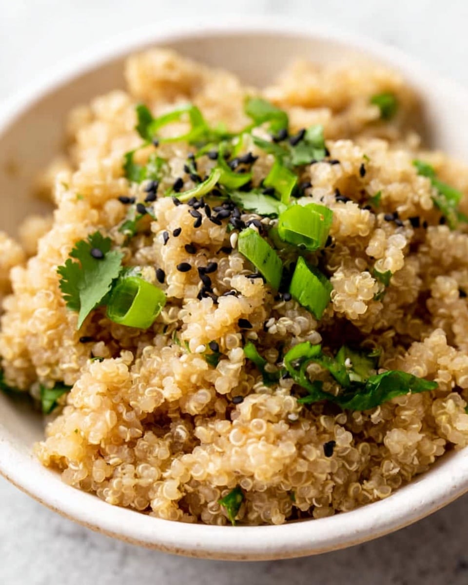A close-up of a white bowl filled with fluffy cooked quinoa that shows small, round grains in a light beige color. The quinoa is topped with scattered black sesame seeds, bright green sliced scallions, and fresh green cilantro leaves. The bowl sits on a white marbled surface, adding a clean, bright background to the dish photo taken with an iphone --ar 4:5 --v 7