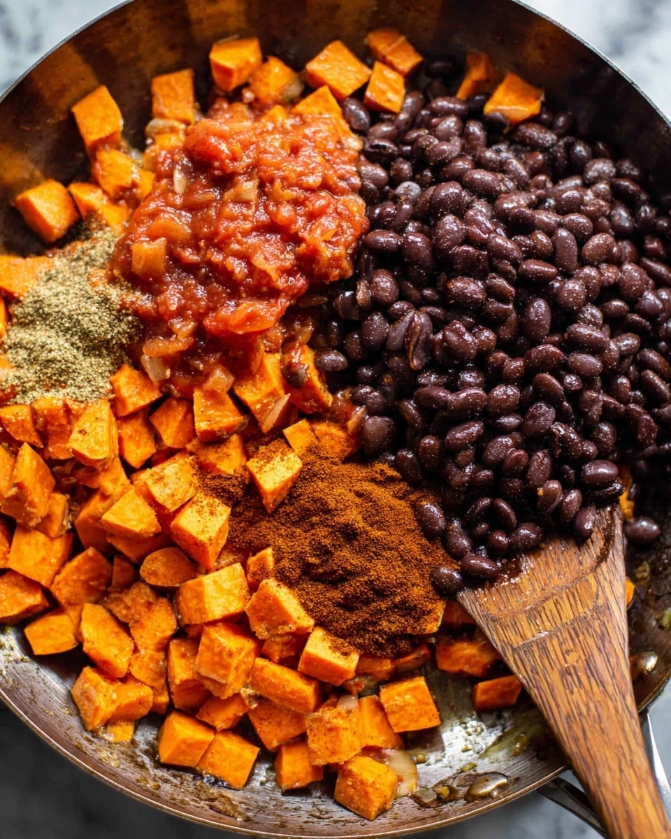 A close-up view of a metal pan filled with four main layers: a base layer of small, cooked orange sweet potato cubes with slight charring on some edges, resting mainly on the right side; a large pile of shiny black beans sits centered above the sweet potatoes; a spoonful of chunky red tomato salsa with visible garlic bits is placed near the upper left; and a small heap of ground cumin and chili powder is near the beans and salsa. A wooden spatula lies on the right side of the pan, partly resting on the sweet potatoes. The background is a white marbled surface. photo taken with an iphone --ar 4:5 --v 7