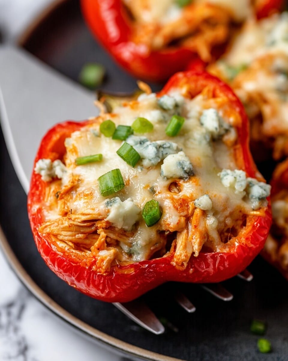 The image shows a close-up of a red bell pepper half stuffed with shredded chicken and topped with melted white cheese and small bits of light blue cheese, garnished with finely chopped green onions. The pepper sits on a metal spatula over a black plate, which holds more stuffed red bell pepper halves blurred in the background. The background surface is a white marbled texture. The layers include the smooth, firm red pepper shell, followed by the moist, stringy chicken filling inside, and the creamy, slightly browned cheese layer on top. Photo taken with an iphone --ar 4:5 --v 7