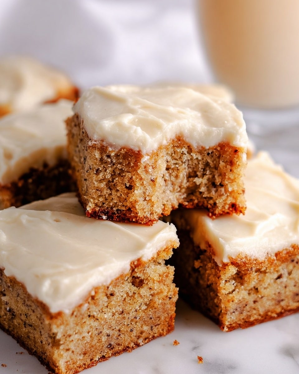 The image shows several square pieces of cake stacked close together. Each piece has two layers: a thick, light brown base with a soft, moist texture and small darker specks, and a smooth, creamy off-white frosting layer on top. The frosting looks thick and slightly swirled, covering the base evenly. One piece in the center has a bite taken out, showing the soft inside of the cake. The background is a white marbled texture, and there is a clear glass with a light-colored drink blurred in the back. photo taken with an iphone --ar 4:5 --v 7