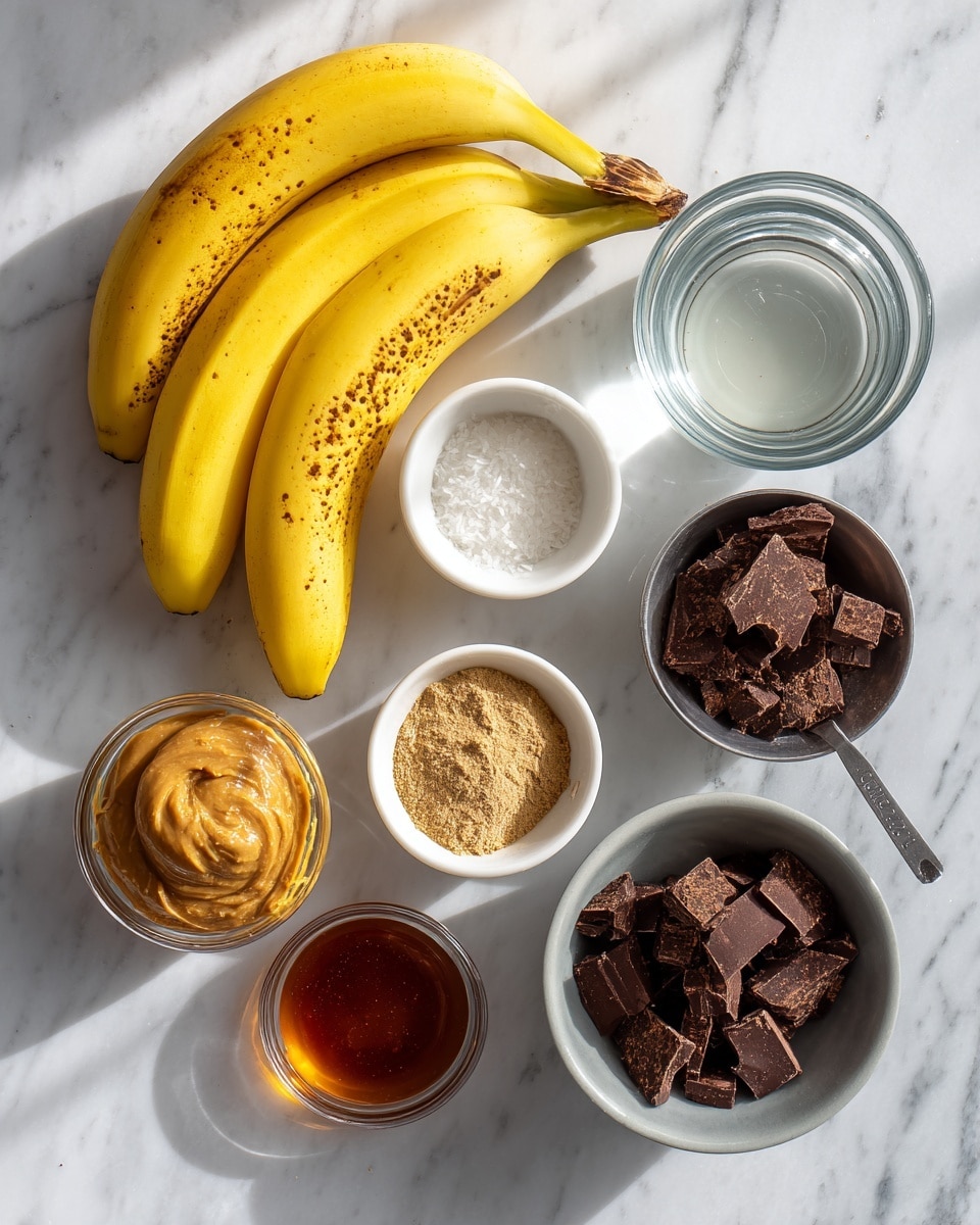 The image shows several ingredients arranged on a white marbled surface. There are three ripe yellow bananas with brown spots on the left side. A small white bowl filled with clear water is at the top center. Below the bananas, a small white bowl contains a tan powder labeled collagen. To the right, a metal measuring cup holds dark brown chunks of chocolate. Below that, a gray bowl has a white scoop of coconut oil. Above the chocolate, a small metal measuring cup has smooth, light brown sunbutter. Next to it, a metal tablespoon contains amber honey. Finally, a small white bowl holds dark vanilla extract. The lighting casts soft shadows, making the ingredients look fresh and natural photo taken with an iphone --ar 4:5 --v 7