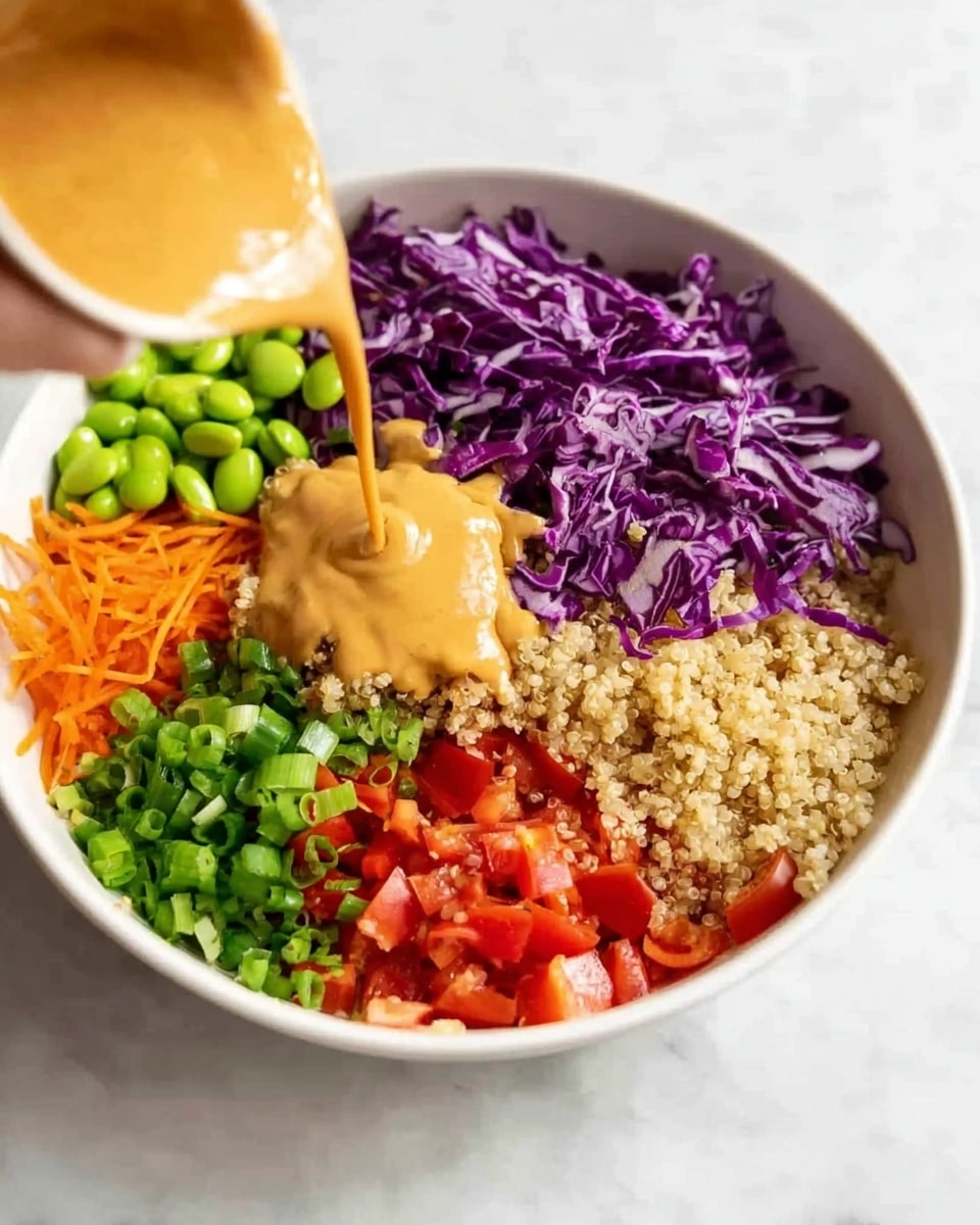 A white bowl sits on a white marbled surface, filled with six colorful layers arranged in sections: shredded purple cabbage in the top left, bright green edamame beans top center, grainy light brown quinoa top right, bright red diced tomatoes bottom right, vibrant green chopped spring onions bottom center, and finely grated orange carrots bottom left. A woman's hand is pouring a smooth, creamy tan sauce over the middle of the bowl, covering parts of the cabbage, quinoa, and carrots. The image captures a fresh and vibrant salad in natural light. photo taken with an iphone --ar 4:5 --v 7