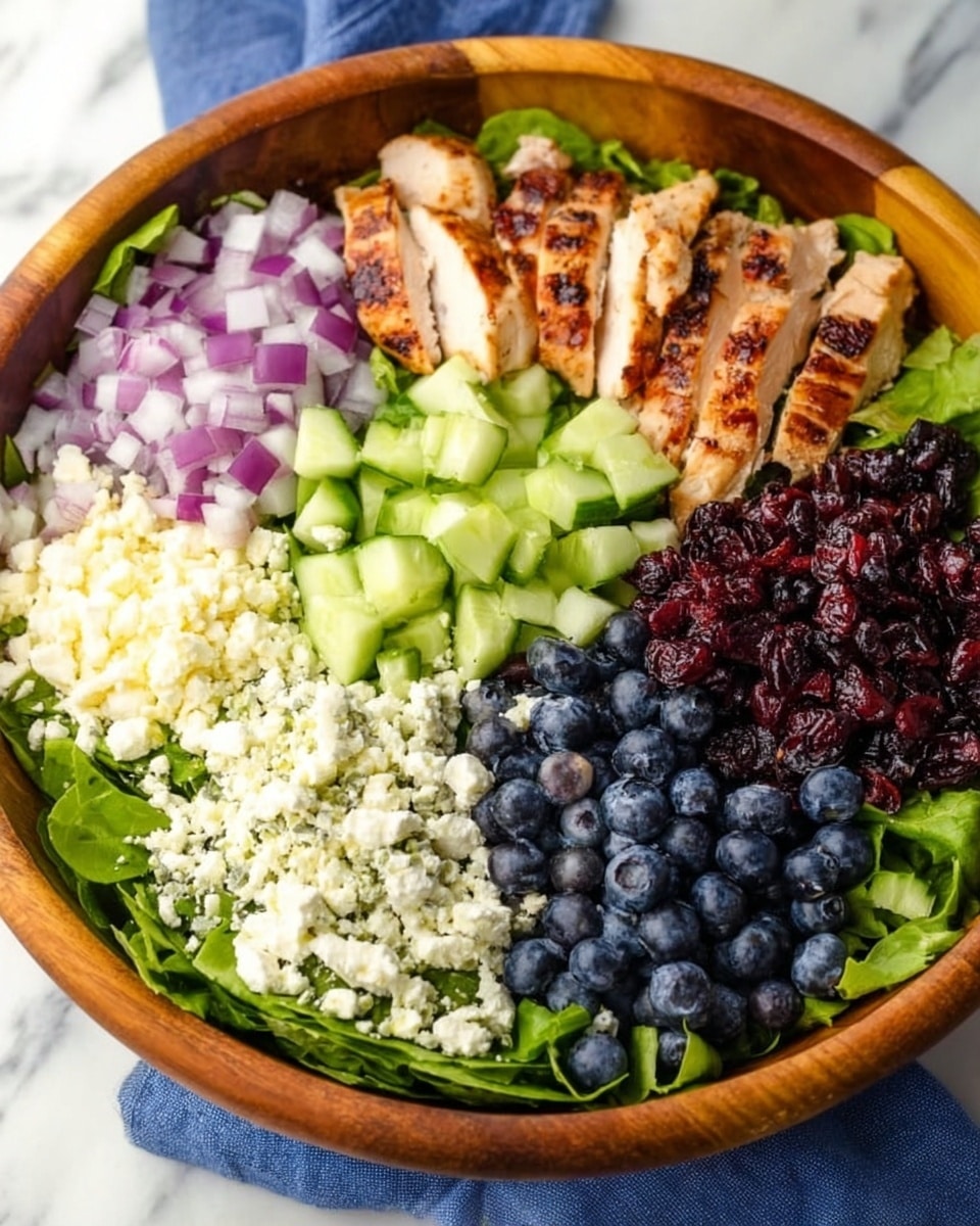 A large wooden bowl contains six layers arranged in sections, each showing different colors and textures. Starting from the top left, there is a layer of small chopped purple onions, next to thin slices of grilled chicken with light brown grill marks. On the top right side, there is a layer of chopped bright green cucumbers. Below the cucumbers, there is a dark red layer of dried cranberries. At the bottom left, there is a layer of white crumbly cheese, and next to it, a layer of dark blue blueberries. All layers rest on a bed of fresh dark green leafy lettuce. The bowl is placed on a white marbled surface with a blue cloth partially visible under the bowl. Photo taken with an iphone --ar 4:5 --v 7