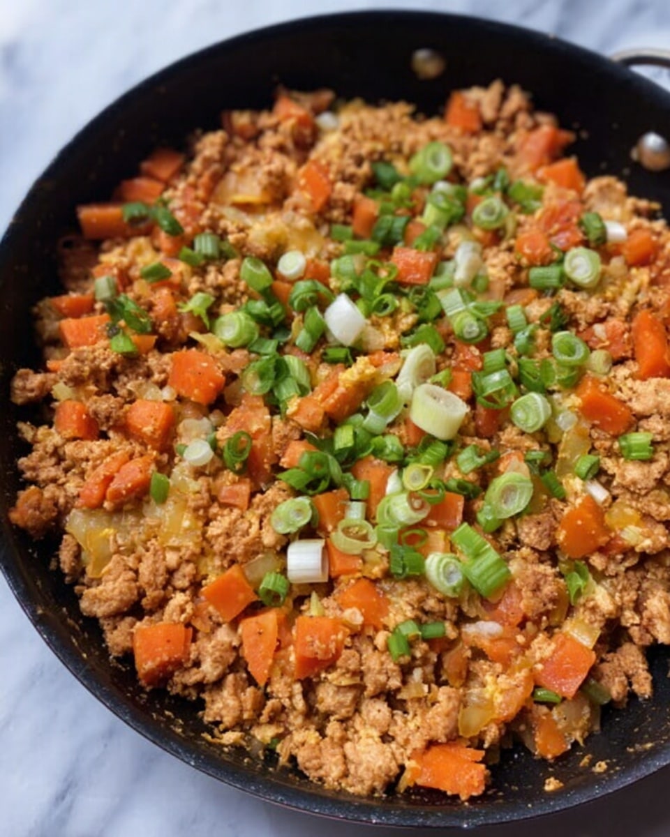 A black pan filled with a dish made of small, crumbly pieces of light brown cooked meat mixed with bright orange carrot chunks. On top, there are chopped green onions with white and light green parts evenly spread across. The pan sits on a white marbled surface with a clear view of the food texture, showing the moist and slightly chunky mix. Photo taken with an iphone --ar 4:5 --v 7