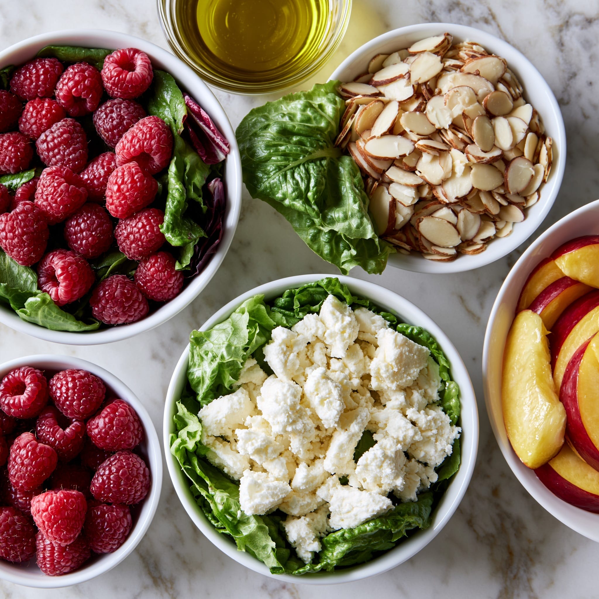 The image shows a white round plate filled with a fresh salad. The bottom layer is a mix of bright green spinach and lettuce leaves. On top are thick slices of red and pale yellow peaches spread evenly. Scattered over the fruit are small red raspberries and white crumbled cheese pieces. There are also thin, light brown almond slices sprinkled around. The plate is placed on a white marbled surface, and in the background, there are whole peaches and a slice of wood. The colors are bright and fresh, making the salad look very inviting. photo taken with an iphone --ar 4:5 --v 7