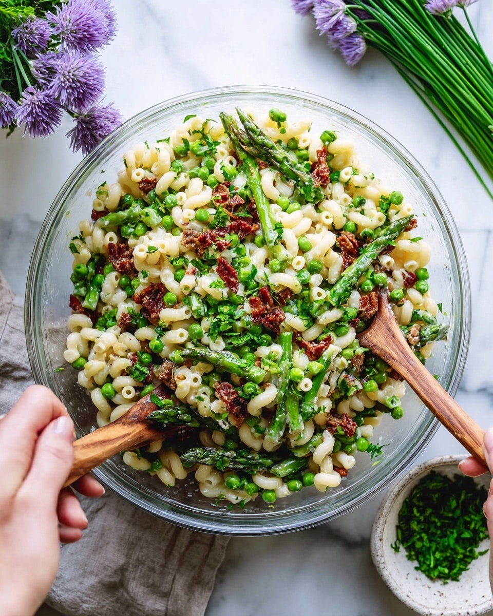 A clear glass bowl holds a colorful pasta salad with three main layers. At the bottom are white elbow macaroni noodles, mixed evenly with bright green peas and thick pieces of fresh asparagus showing a sturdy texture and different shades of green. Throughout the salad are small bits of deep red sun-dried tomatoes adding contrast. On top, finely chopped fresh green herbs and parsley add a sprinkle of freshness. Two wooden spoons are stirring the salad, each held by a woman's hand, and the bowl is placed on a white marbled surface beside a rustic white bowl with chopped herbs and a bunch of purple chive flowers. Photo taken with an iphone --ar 4:5 --v 7