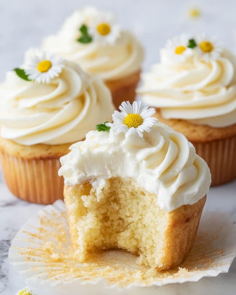 A close-up of four vanilla cupcakes on a white marbled surface, each topped with a thick swirl of white frosting. One cupcake in the front has its white wrapper peeled back and a bite taken out, revealing soft, light yellow cake inside. On top of each cupcake sits a small daisy-like flower with white petals and a yellow center, adding a fresh touch. The frosting looks smooth and creamy with swirling peaks. The scene is softly lit, emphasizing the delicate texture of the cake and frosting. photo taken with an iphone --ar 4:5 --v 7