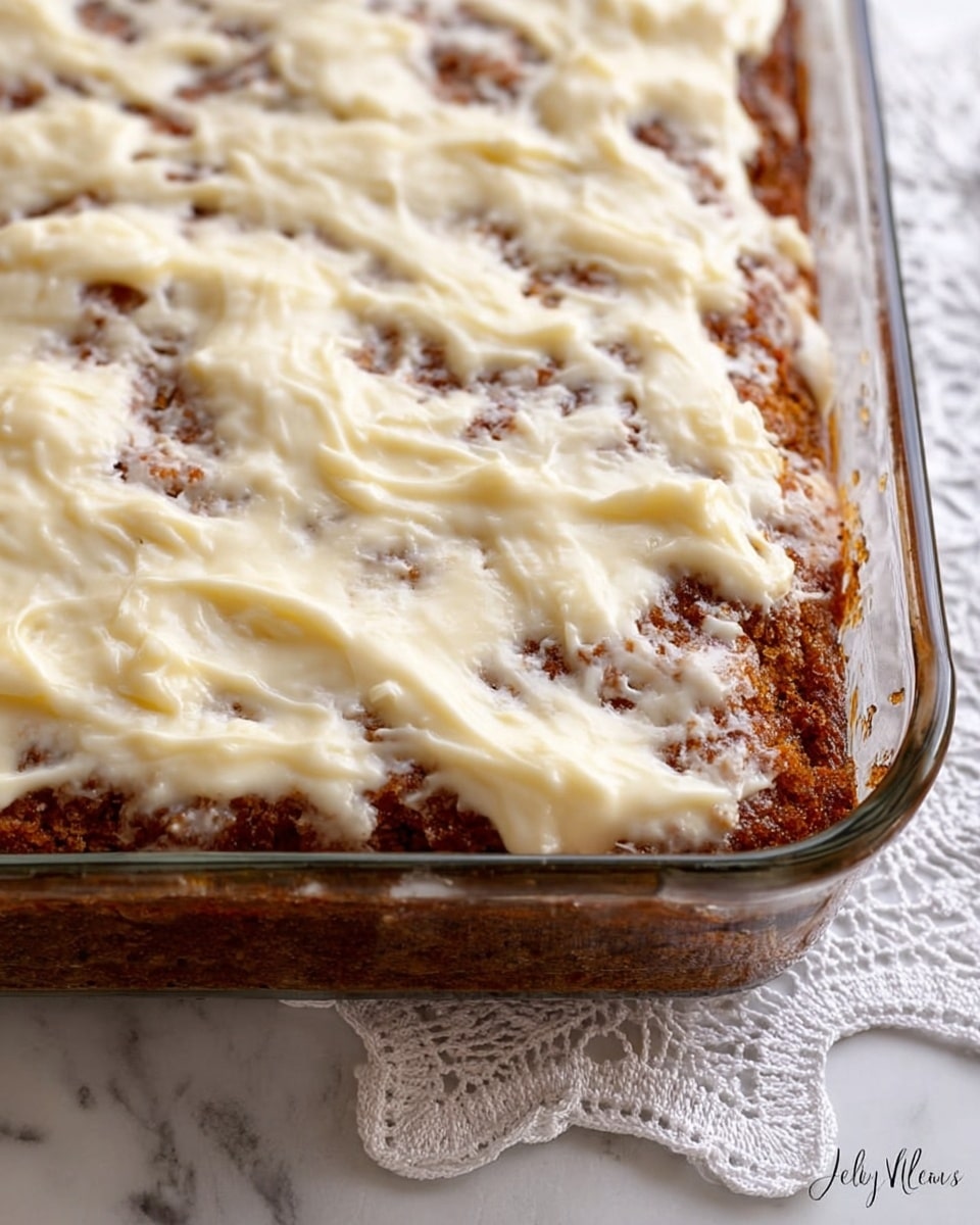 A close-up view of a rectangular glass baking dish filled with a two-layer dessert. The bottom layer is a dark golden brown cake with a slightly rough texture visible through the top layer. The top layer is a smooth, creamy off-white icing unevenly spread over the cake, showing some parts of the cake underneath. The dish rests on a white marbled surface with a lace tablecloth partially visible under it. photo taken with an iphone --ar 4:5 --v 7